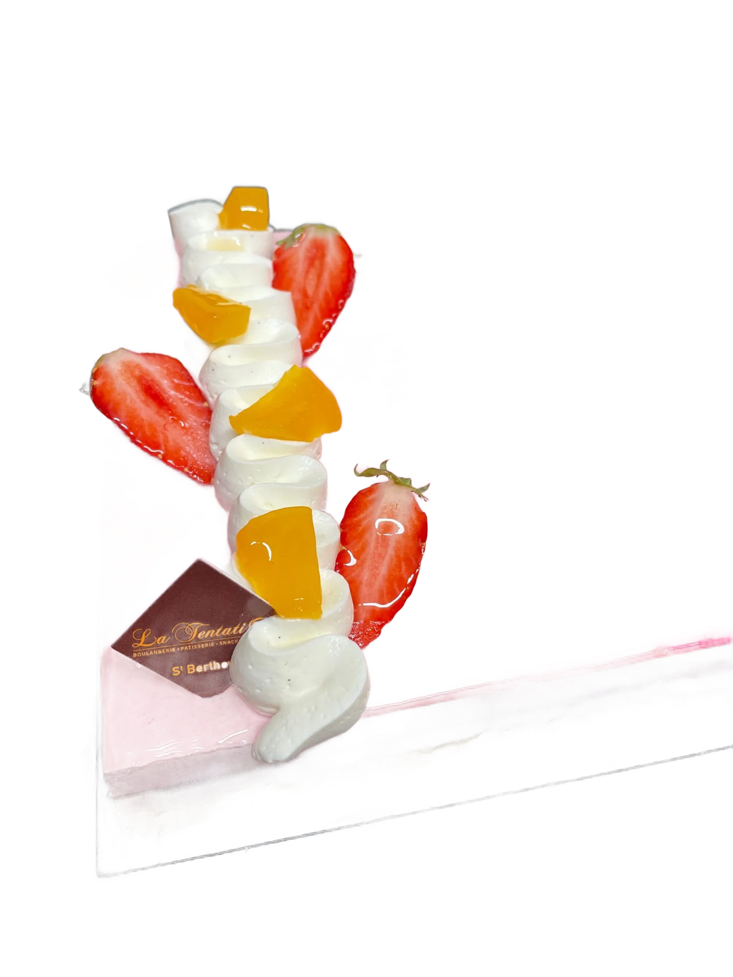 Entremets carré au glaçage rose, décoré de fraises, de chantilly et de morceaux de mangue.