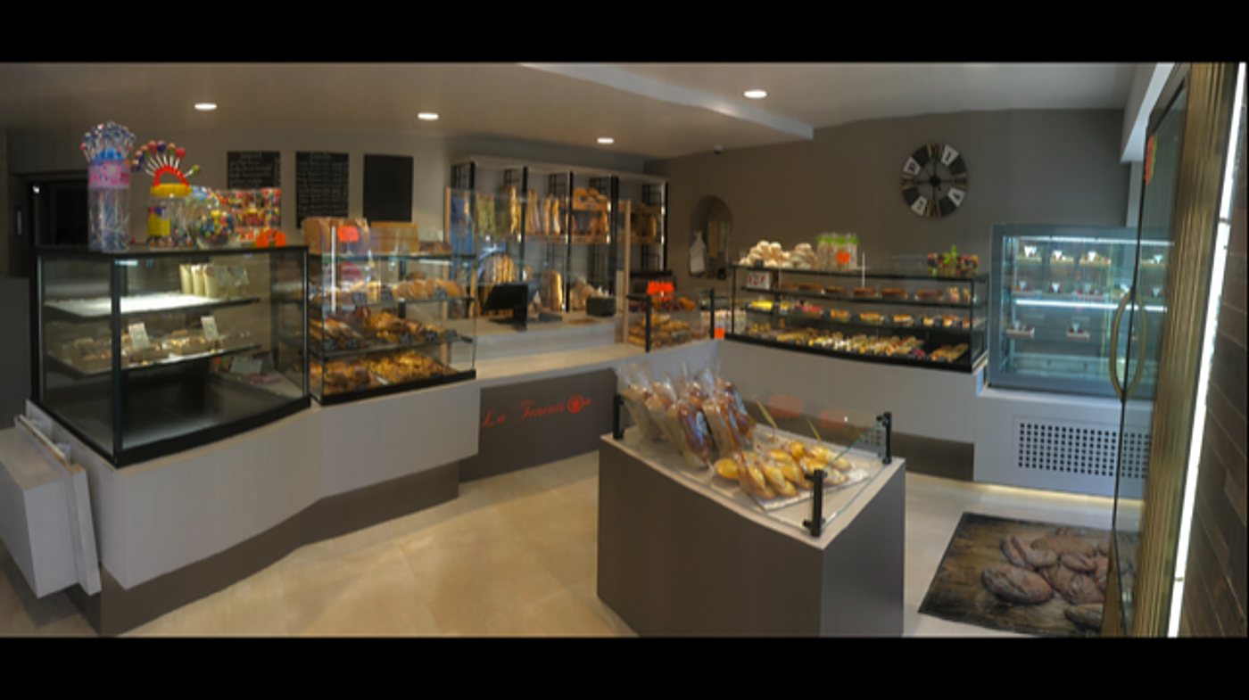 Intérieur lumineux de la boulangerie-pâtisserie, avec des vitrines de viennoiseries et de gâteaux et un présentoir à pains.