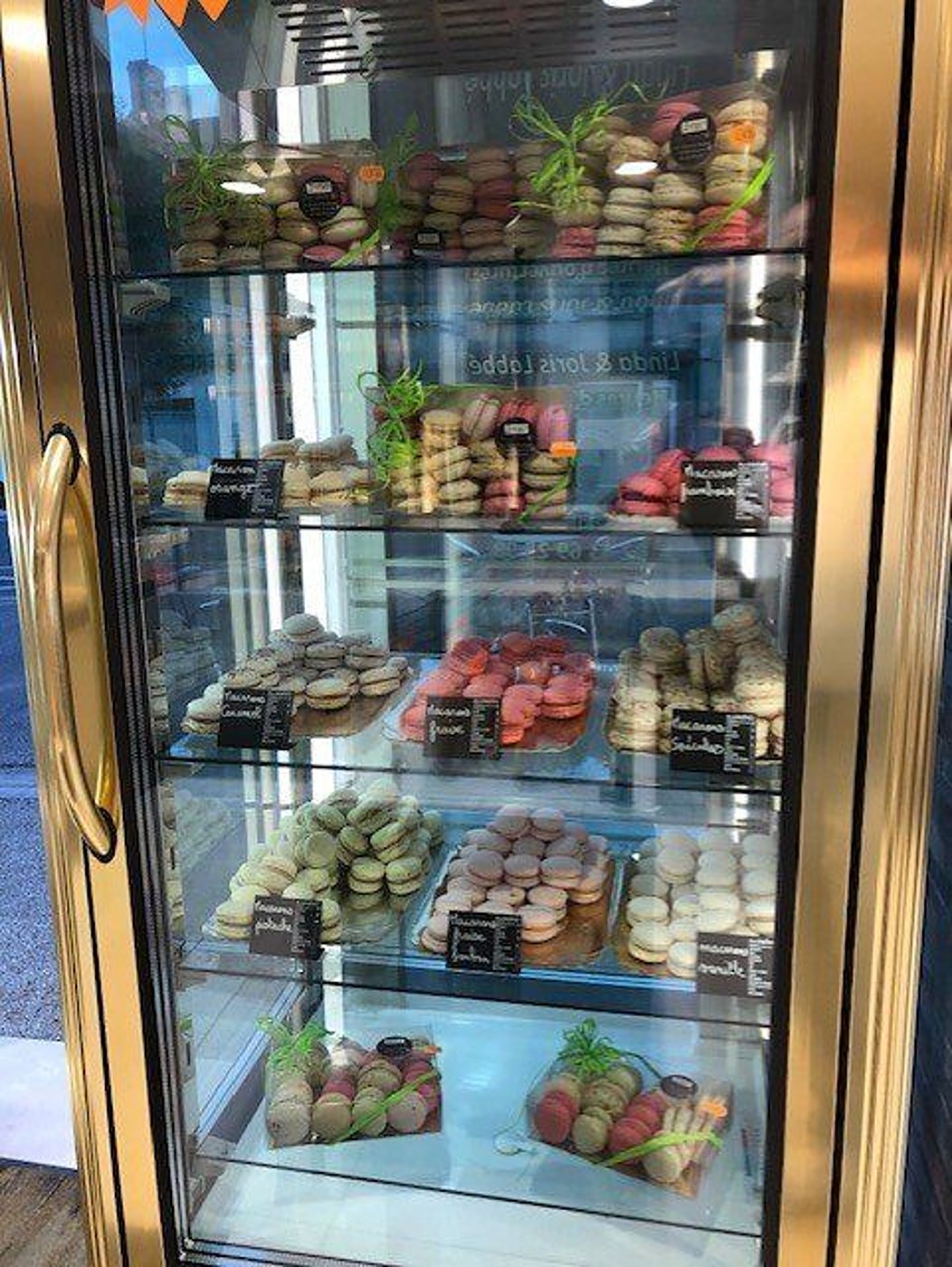 Vitrine réfrigérée remplie de macarons de toutes les couleurs, rangés par parfum sur plusieurs étagères.